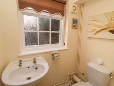 A bathroom with a sink under a textured window and a toilet with wall art at Winkle Cottage Aldeburgh