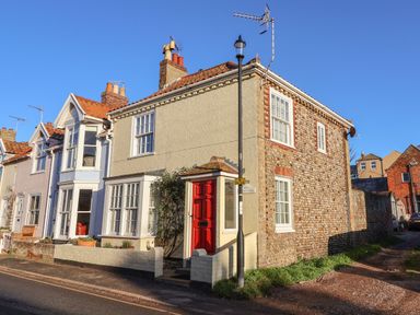 A row of two story houses with a red door and chimneys on a street at Winkle Cottage Aldeburgh