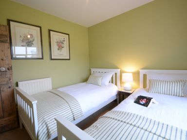 A bedroom with two single beds white bedding striped blankets and pillows bedside table with lamp and framed floral prints on the wall at Rookyards Spexhall Near Halesworth