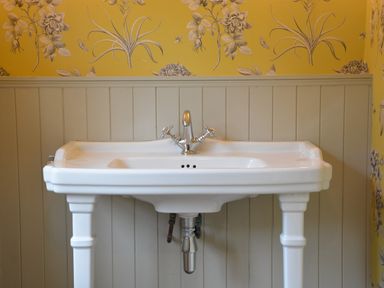 A white pedestal sink with chrome taps against a wall with beige paneling and yellow floral wallpaper at Rookyards Spexhall Near Halesworth