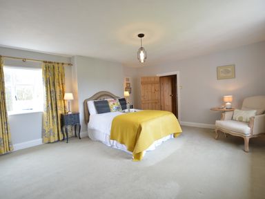 A bedroom with a bed with yellow blanket curtains by the window bedside tables with lamps an armchair and wooden door at Rookyards in Spexhall Near Halesworth