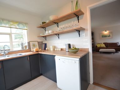 A kitchen with wooden countertops open shelves with dishes and glassware and a white dishwasher at Rookyards Spexhall Near Halesworth