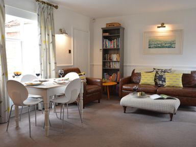A living room with a dining table set near a window a brown leather sofa and armchair a bookshelf and an ottoman at Rookyards Spexhall Near Halesworth
