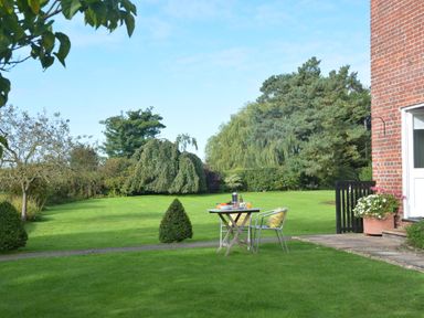 A garden with a table and two chairs set with breakfast near a brick house at Rookyards Spexhall Near Halesworth