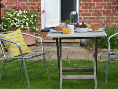 An outdoor table set with breakfast items and two metal chairs on grass at Rookyards Spexhall Near Halesworth