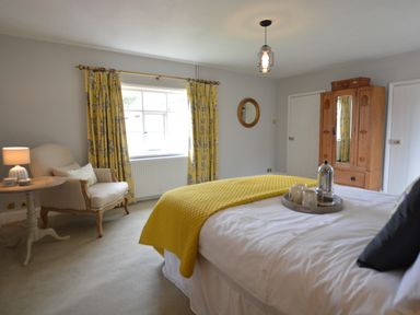 A bedroom with a bed with a yellow blanket an armchair with a side table a wooden wardrobe and yellow curtains at Rookyards Spexhall Near Halesworth