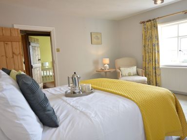 A bedroom with a yellow bedspread a gray pillow a wooden chair a window with yellow curtains and a wooden door at Rookyards in Spexhall Near Halesworth