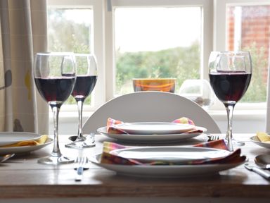 A dining table set with plates forks napkins and glasses of red wine in front of a window at Rookyards Spexhall Near Halesworth