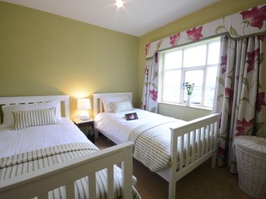 A bedroom with two single beds a bedside table with lamp and a window with floral curtains at Rookyards Spexhall Near Halesworth