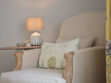 A beige armchair with a decorative pillow and a side table with a lamp and small dishes at Rookyards Spexhall Near Halesworth