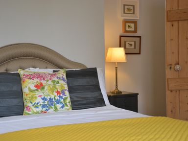 A bedroom with a bed with floral and dark pillows a yellow blanket a bedside table with a lamp and bird pictures on the wall at Rookyards Spexhall Near Halesworth
