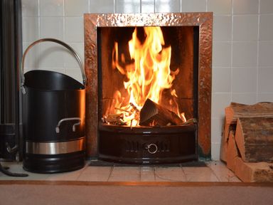 A burning fire in a fireplace with a metal bucket and stacked firewood beside it at Rookyards Spexhall Near Halesworth