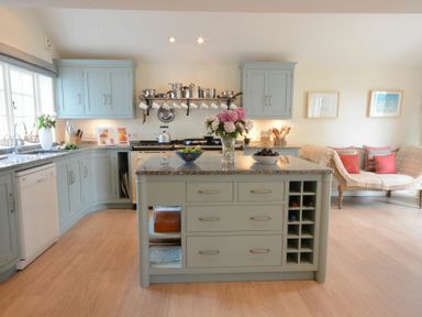 A kitchen with blue cabinets an island with flowers and bowls and a seating area with a bench at 2 The Bays Thorpeness