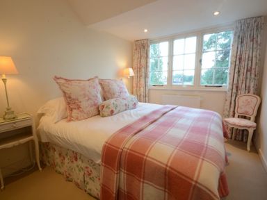 A bedroom with a bed covered by a pink checkered blanket two bedside tables with lamps and floral curtains at 2 The Bays Thorpeness