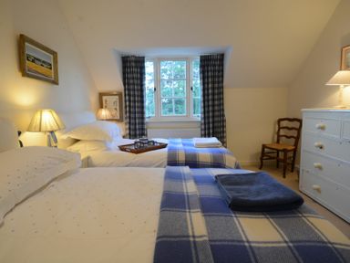 A bedroom with two single beds with blue plaid blankets a window with curtains and a white dresser at 2 The Bays Thorpeness