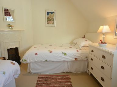 A bedroom with two beds a white dresser with a lamp and a small fireplace at 2 The Bays Thorpeness