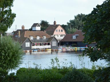 A waterfront scene with boats docked by houses surrounded by trees at 2 The Bays in Thorpeness