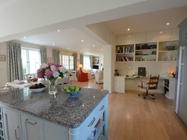 A kitchen island with fruit bowls and flowers next to a dining area and a home office desk with shelves at 2 The Bays Thorpeness