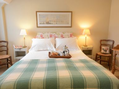 A bedroom with a bed with a floral headboard a green and white blanket two bedside tables with lamps and wooden chairs at 2 The Bays Thorpeness