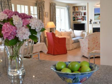 A living room with a sofa armchairs a table with a lamp and built in bookshelves with a tv a bowl of green apples and a vase of flowers at 2 The Bays Thorpeness