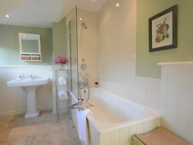 A bathroom with a bathtub a sink a glass shelf with towels and flowers and a framed picture on the wall at 2 The Bays Thorpeness