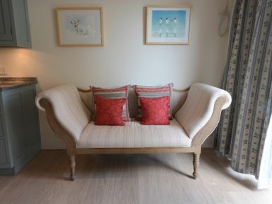 A wooden framed upholstered sofa with four cushions under two framed pictures at 2 The Bays Thorpeness