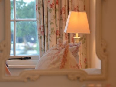 A window with floral curtains a table lamp and cushions reflected in a mirror at 2 The Bays Thorpeness