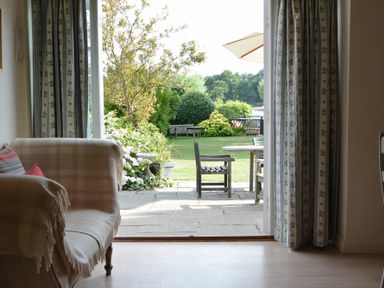 A living room with a sofa and curtains opening to a garden with chairs and a table at 2 The Bays Thorpeness