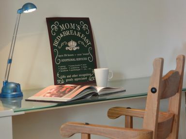 A glass desk with a wooden chair a blue lamp an open book a white mug and a decorative sign at 2 The Bays Thorpeness