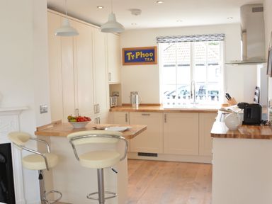 A kitchen with bar stools a fruit bowl and a Ty-Phoo tea sign on the wall at 4 The Dunes Thorpeness