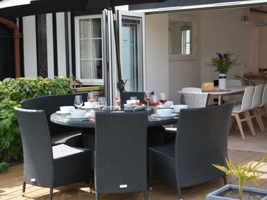 An outdoor dining area with a round table set with bowls and glasses and black wicker chairs at 4 The Dunes Thorpeness