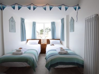 A bedroom with two single beds with folded towels on them and a window with blue curtains at 4 The Dunes Thorpeness
