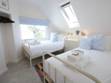 A bedroom with two single beds white linens blue pillows a window and a skylight at 4 The Dunes Thorpeness