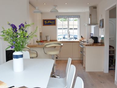 A kitchen with a dining table and chairs flowers on the table and bar stools at 4 The Dunes Thorpeness