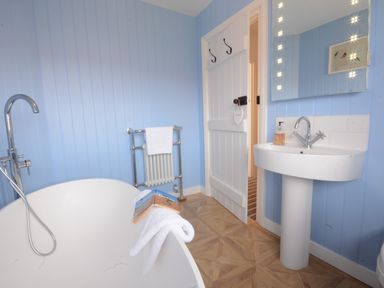 A bathroom with a freestanding bathtub a towel on radiator a pedestal sink and mirror at 4 The Dunes Thorpeness
