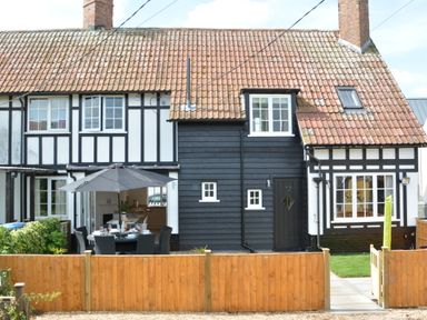 A Tudor-style house exterior with black and white paneling a red tiled roof a wooden fence and an outdoor dining table with umbrella at 4 The Dunes Thorpeness