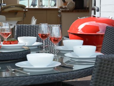 An outdoor dining table with white bowls plates and glasses of rose wine next to a red barbecue grill at 4 The Dunes Thorpeness