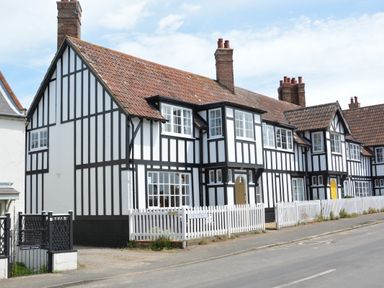 A row of black and white timber framed houses with white picket fences along a street at 4 The Dunes Thorpeness