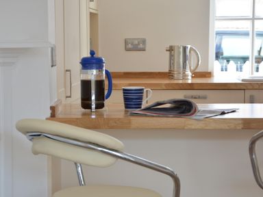 A kitchen counter with a coffee press, a striped mug, and a newspaper with a chair in the foreground at 4 The Dunes Thorpeness