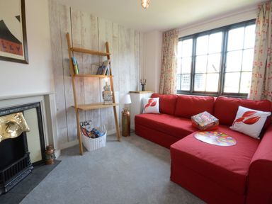 A living room with a red sofa two pillows a ladder shelf and a fireplace at 4 The Dunes Thorpeness