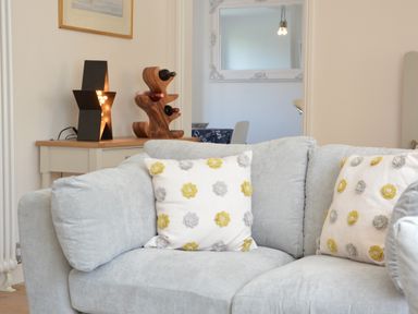 A corner of a living room with a grey sofa and flower patterned cushions at 4 The Dunes Thorpeness