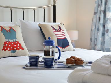 A bed with decorative cushions coffee pot cups muffins and folded towels at 4 The Dunes Thorpeness