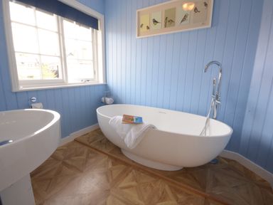A bathroom with a white freestanding bathtub a pedestal sink a window and blue paneled walls at 4 The Dunes Thorpeness