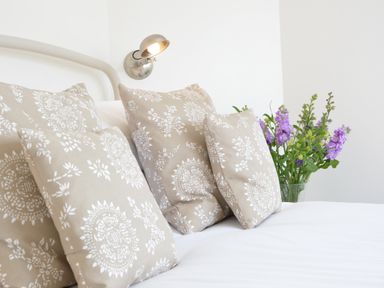 A bed with beige patterned pillows and purple flowers in a vase at 4 The Dunes in Thorpeness