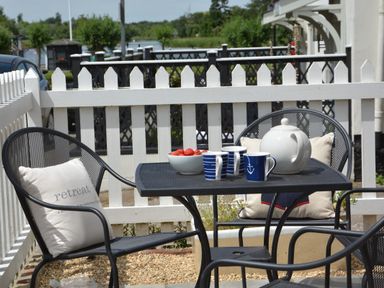 A patio with a black metal table and chairs with cushions a teapot cups and a bowl of strawberries by a white picket fence at 4 The Dunes Thorpeness