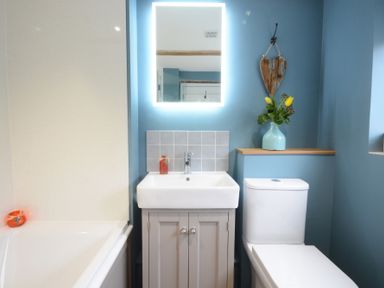 A bathroom with a bathtub sink toilet a mirror with light and flowers in a vase at 1 The Old Coach House in Huntingfield Near Laxfield
