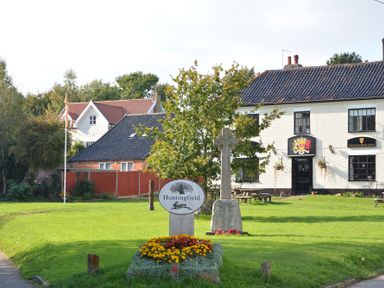 A village green with a war memorial and a sign saying Huntingfield in front of white buildings at 1 The Old Coach House Huntingfield Near Laxfield