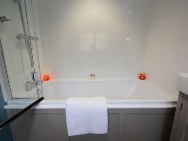 A bathroom with a bathtub white towel candles and toiletries at 1 The Old Coach House Huntingfield Near Laxfield