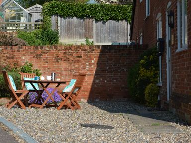 An outdoor seating area with a wooden table and chairs on gravel near a brick wall at 1 The Old Coach House Huntingfield Near Laxfield