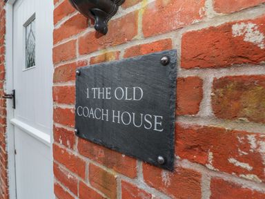 A brick wall with a black plaque reading 1 The Old Coach House next to a white door at 1 The Old Coach House Huntingfield Near Laxfield